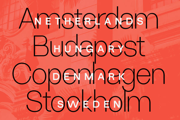 SLTF Ryecroft specimen on a coral red ground with a faint architectural photograph showing through. Four city names - Amsterdam, Budapest, Copenhagen and Stockholm - are set very large in the thinnest weight in black outline. Overlapping them in bold white letterspaced capitals are the matching countries: Netherlands, Hungary, Denmark and Sweden. The two layers cross without either becoming unreadable.