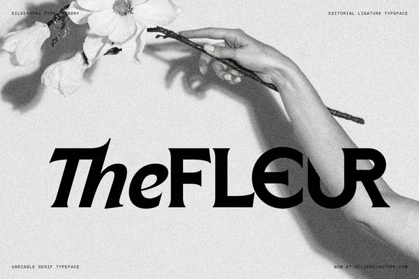 SLTF Arcilla Black Italic specimen — the word TheFLEUR set at display size in solid black against a black and white photograph of a hand holding a delicate flower branch. Highlights the expressive calligraphic quality of the italic cut and the ligature between lowercase letters at large sizes.
