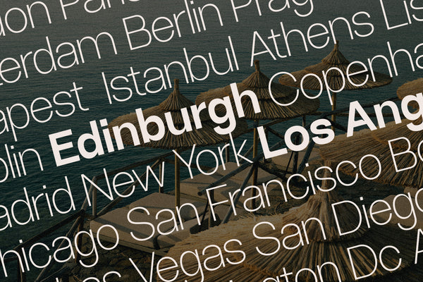 SLTF Ryecroft specimen over an angled photograph of thatched beach umbrellas and loungers above dark sea water. City names are layered across the frame in a light cream weight - Amsterdam, Berlin, Prague, Budapest, Istanbul, Athens, Copenhagen, Madrid, New York, Chicago, San Francisco, Las Vegas and San Diego - with Edinburgh and Los Angeles set in bold to break up the field.