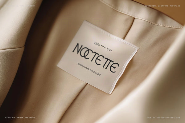 SLTF Arcilla Regular used in the Noctette luxury fashion brand — a woven care label photographed inside the lining of a camel-coloured coat. The label reads ESTD 1972 / NOCTETTE / WHERE ELEGANCE MEETS EDGE. A refined example of Arcilla in premium apparel branding, labels, and luxury goods identity design.
